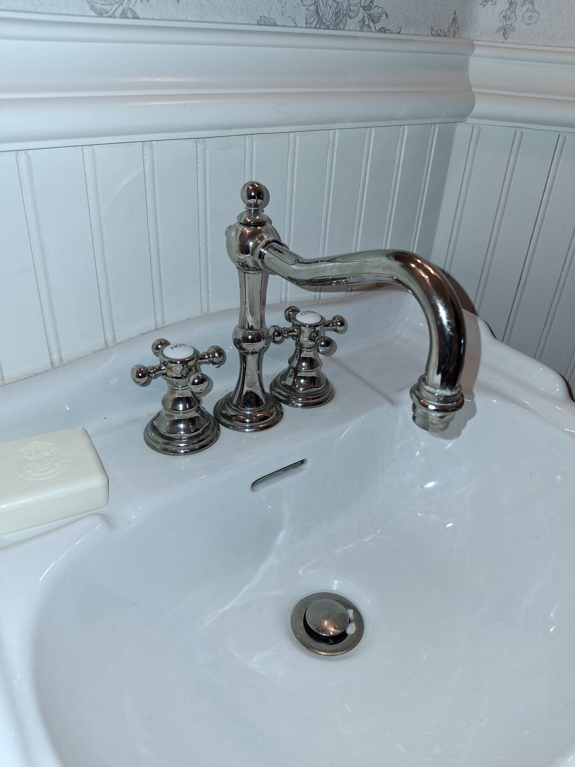 White porcelain sink with chrome faucet and handles, soap bar on the left, and beadboard paneling on the wall behind.